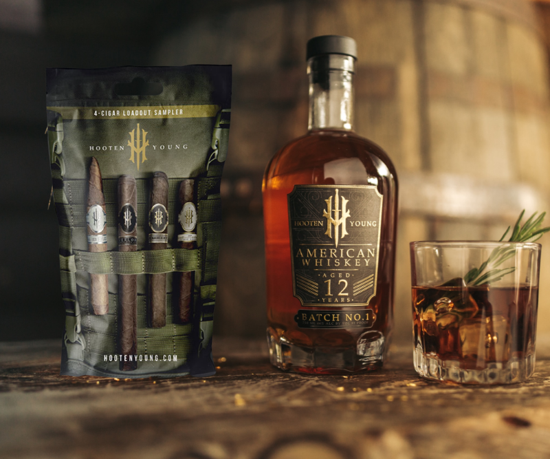 Hooten Young 12 Year whiskey bottle with 4-cigar Loadout sampler pack and whiskey glass with rosemary garnish on wooden surface